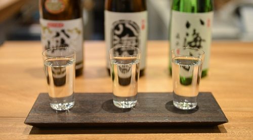A row of glasses containing sake with the bottles in the background