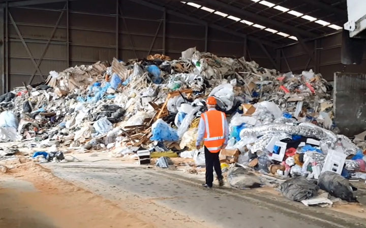 a lone waste management worker walks toward a pile of plastic waste